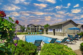 A pool surrounded by lawn chairs and flowers with a building in the background.